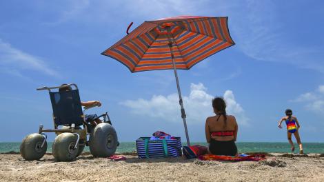 坐在沙滩轮椅上,在佛罗里达州比斯坎湾的无障碍海滩上享受阳光与海 坐在沙滩轮椅上,在佛罗里达州比斯坎湾的无障碍海滩上享受阳光与海